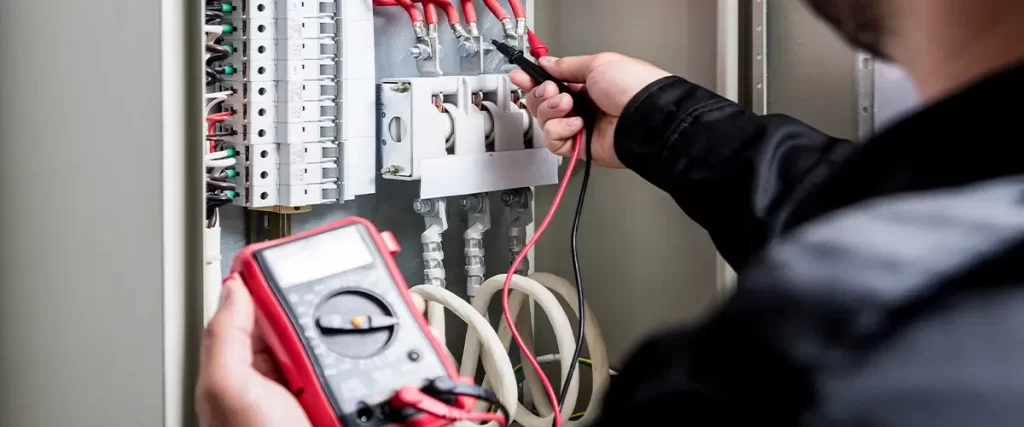 Technician inspecting electrical panel wiring with a multimeter for safety and efficiency in a commercial setup.