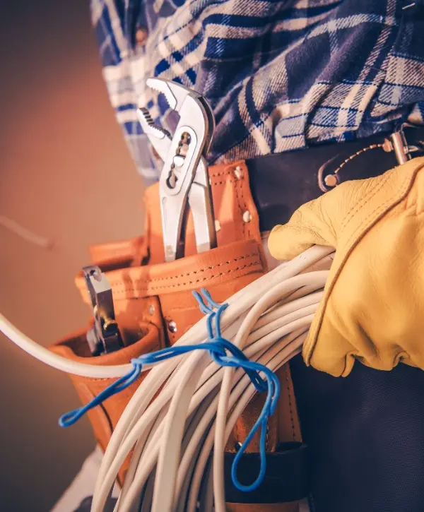 A man holds a wrench in one hand and cables in the other, ready for an electrical task