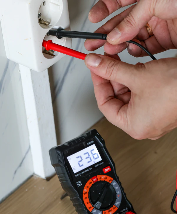 An electrician using a digital multimeter to test voltage at a white wall outlet for general electrical repair in Center Valley, PA.