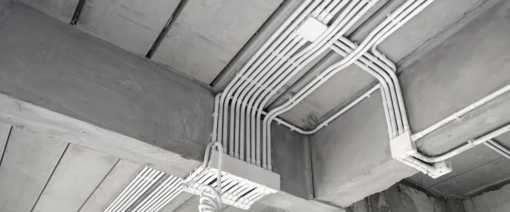 Multiple parallel runs of white PVC electrical conduit mounted neatly across a raw concrete ceiling and structural beams in a modern building.